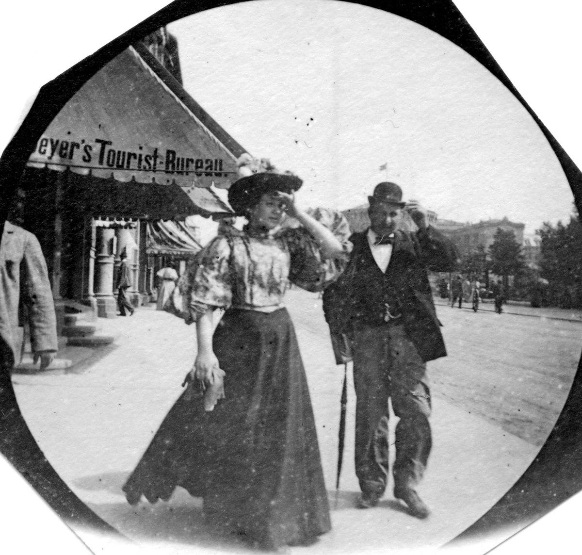 Fredrik Carl Mülertz Størmer, Mann og kvinne spaserer langs Karl Johans gate, Oslo. Markise merket "Beyer`s Tourist- Bureau".