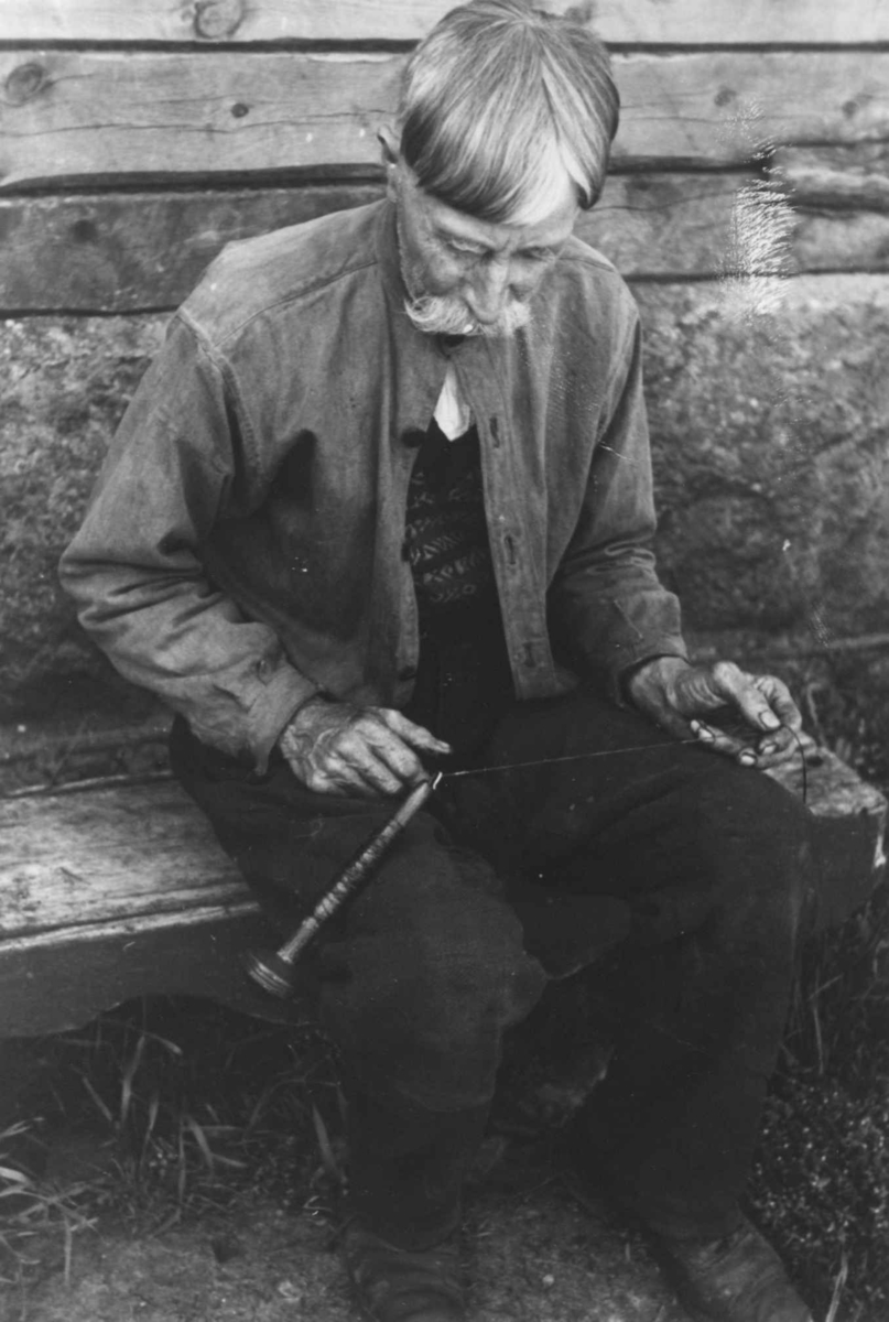Anna Grostøl, En mann sitter med en håndtein og lager skomakertråd. Åseral, Vest-Agder 1943.