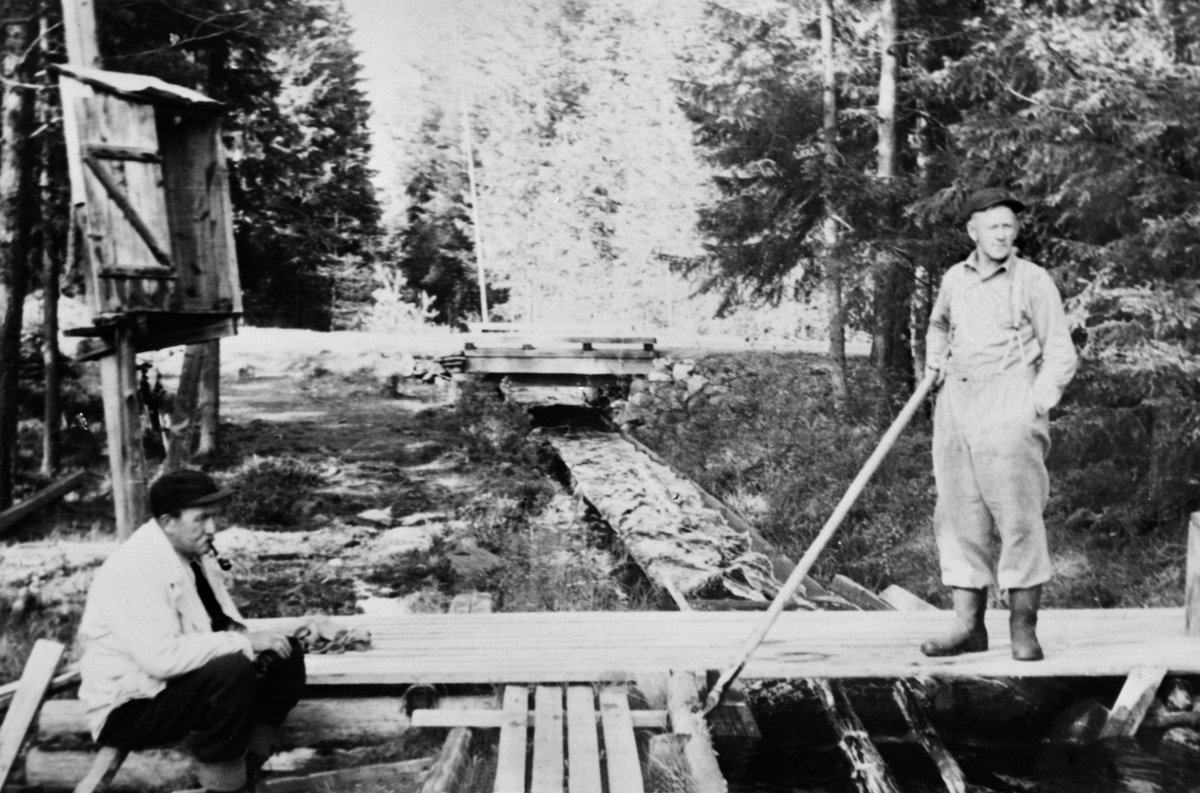 Anno Domkirkeodden, STENSÅSRENNA, TØMMERFLØTING, FRA VENSTRE: SKOGBESTYRER ALBERT NORDSVEEN OG EIVIND SOLBERG, TØMMERRENNER. "I bakgrunnen på bildet ser vi Rennebrua som har gitt opphav til stedsnavnet. Denne brua var en del av hovedveien til Østre Skogbygd. Bestyrer Albert Nordsveen slapper av med ei god pipe, mens E…