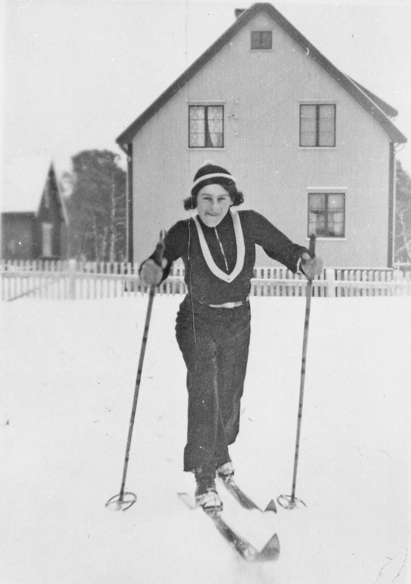 Rachel Haarseth, Kvinne, klær, ski og skistaver, gjerde, bygning.