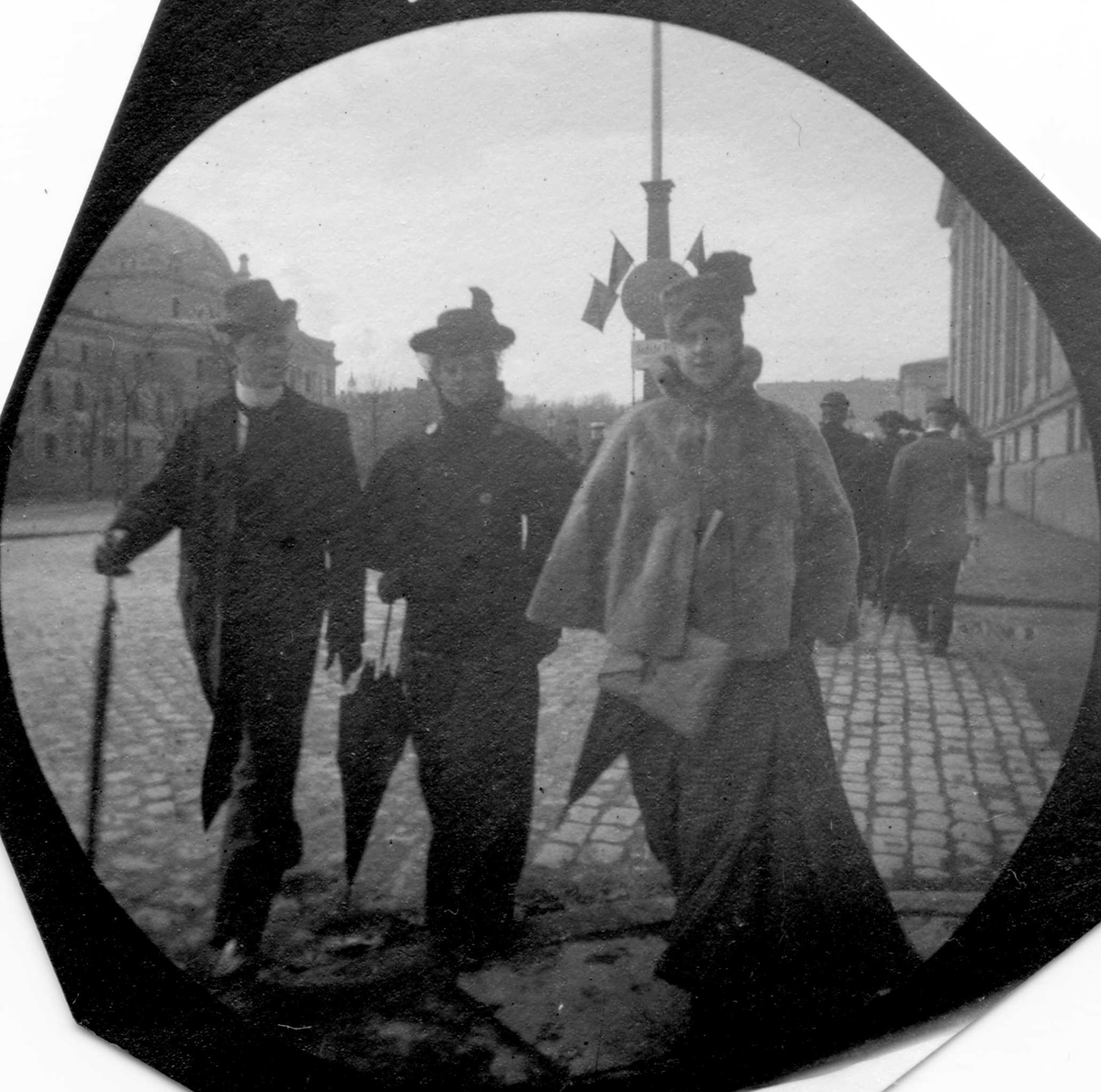 Fredrik Carl Mülertz Størmer, Jens Z. Kielland, frk. Baby Kielland og frk. Nina Thaulow spaserer langs Karl Johans gate, Oslo, med Nationaltheatret og Universitetet på hver side.