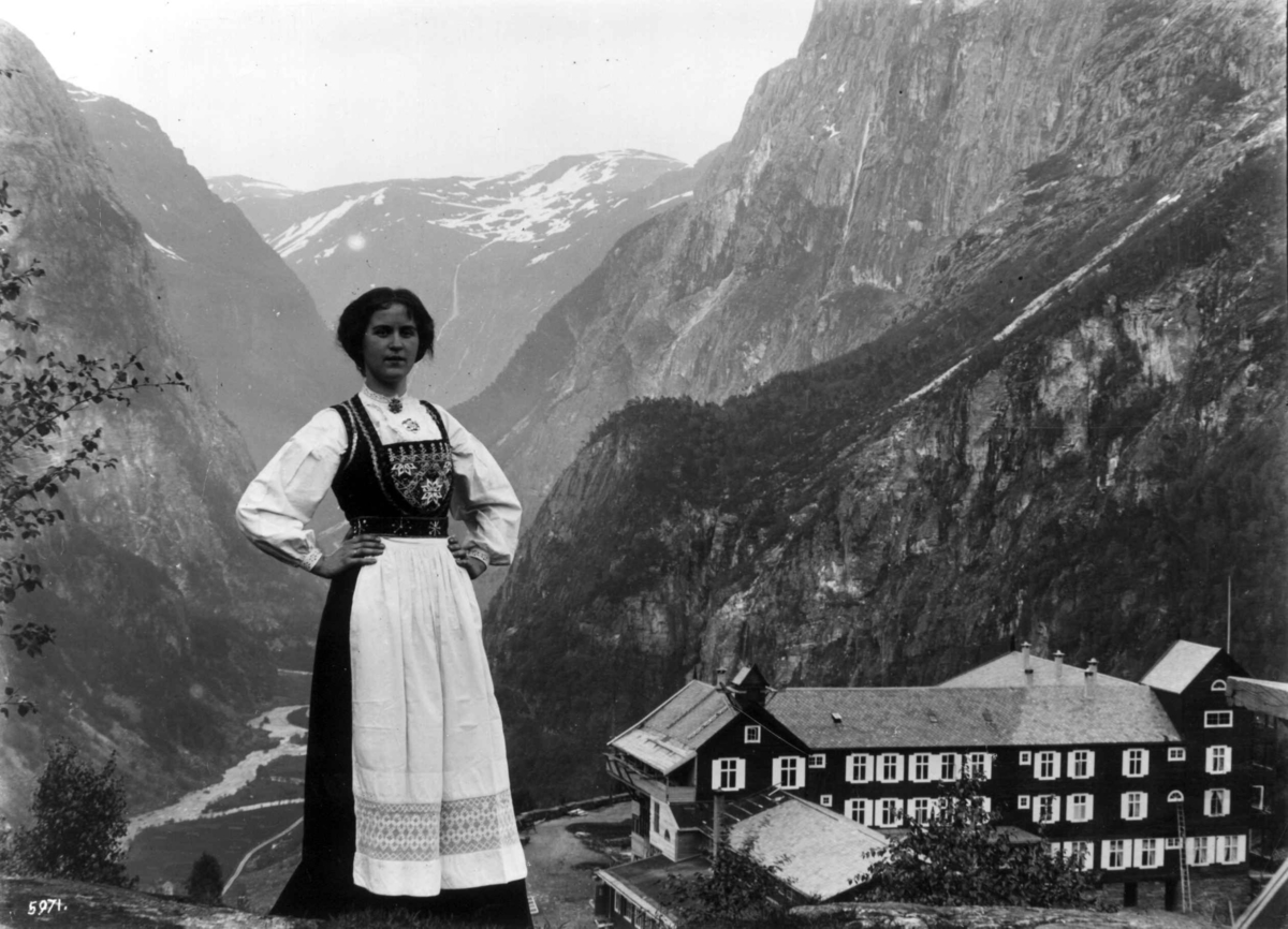 Hermann Christian Neupert, Stalheim Hotel, Voss, Hordaland. I forgrunnen en kvinne i folkedrakt. Hotellet til høyre. I bakgrunnen Nærøydalen med elv, fjell og fossefall.