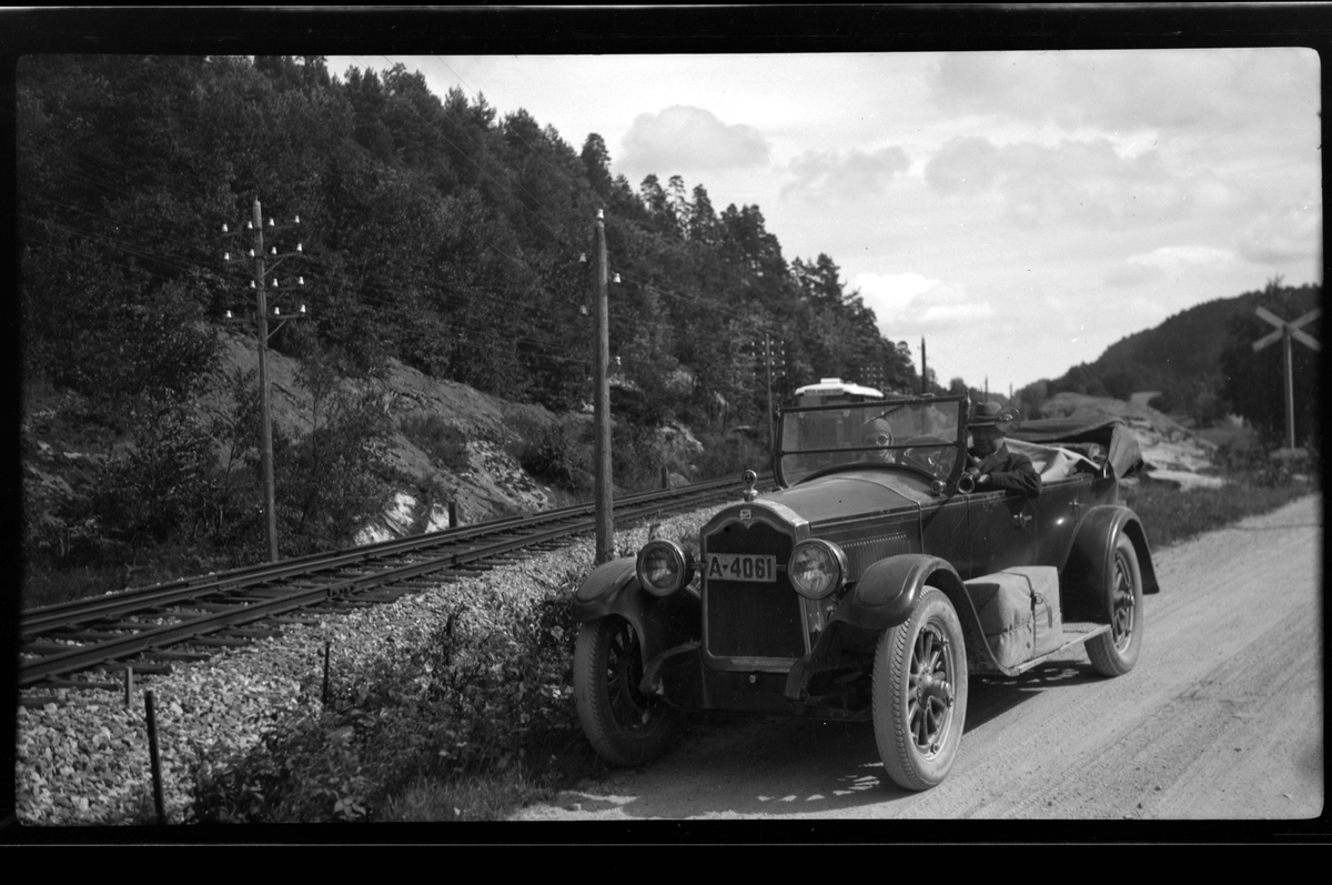 Rolf Sr. Sundt, Far og sønn Rolf Sundt sitter i bilen ved Flaksvannbanen i Lillesand, med strømmaster, jernbanespor og skog i bakgrunnen.