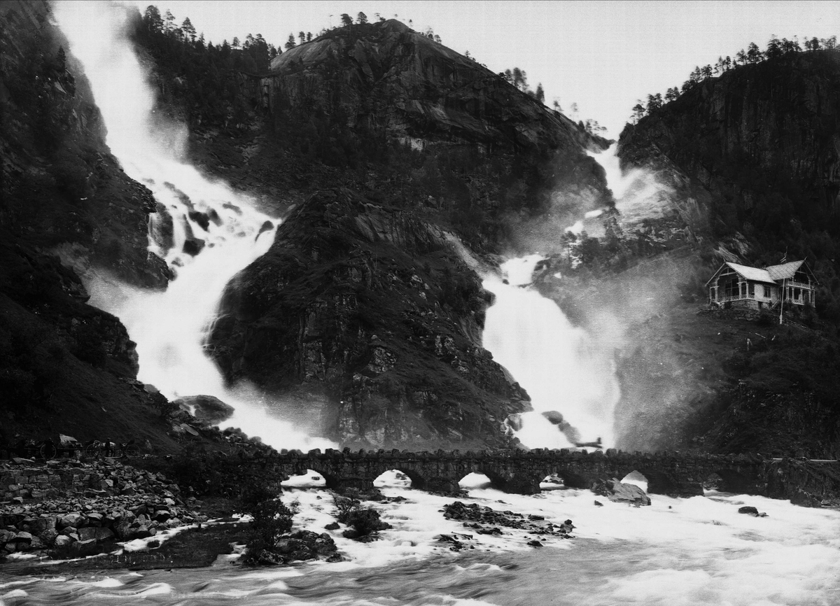 Solveig Lund, Landskapsfotografi. Fossefall med bro nedenfor. Hus til høyre i bildet.