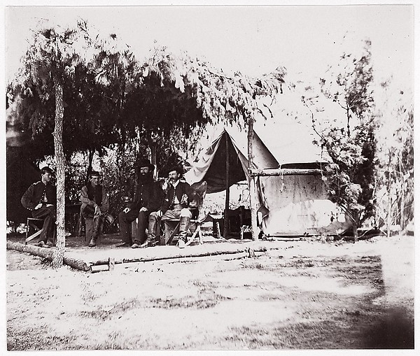 Unknown, [Four men in camp under a lean-to of pine boughs]