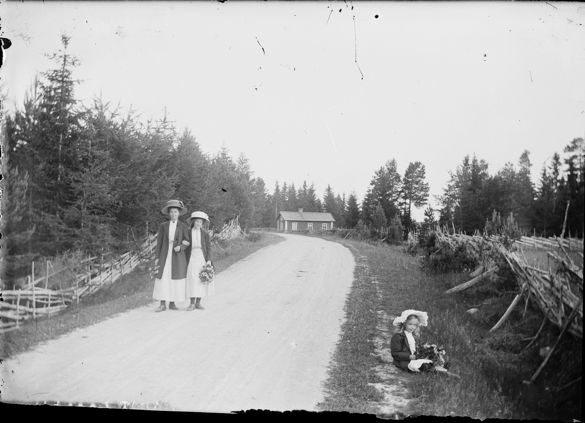 Skötsner-Edhlund, Promenerande kvinnor med blommor. Flicka sitter i vägkanten med blommor i händerna, Östhammar, Uppland. Tidigt 1900-tal.