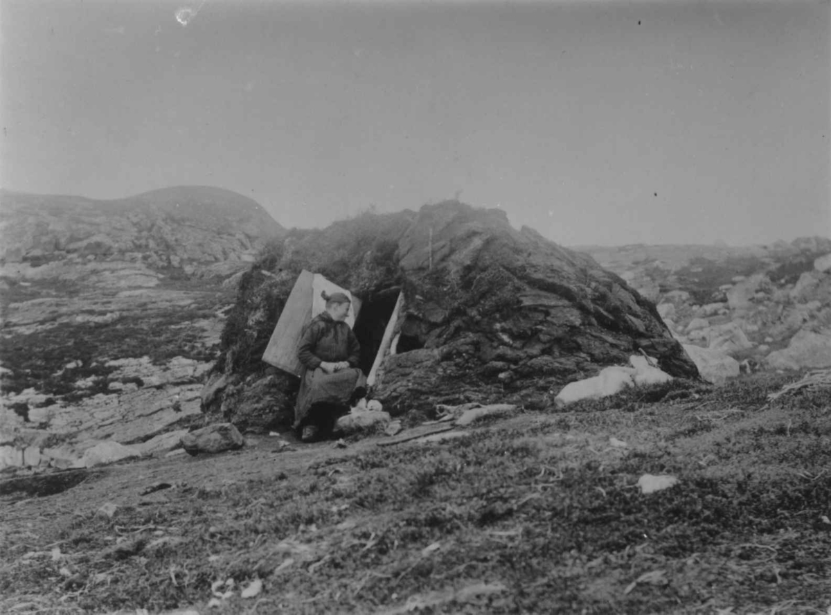 Ellisif Rannveig Wessel, En kvinne sitter i døråpningen til en torvgamme, Skogerøya, Sør-Varanger, Finnmark, 1890-årene.