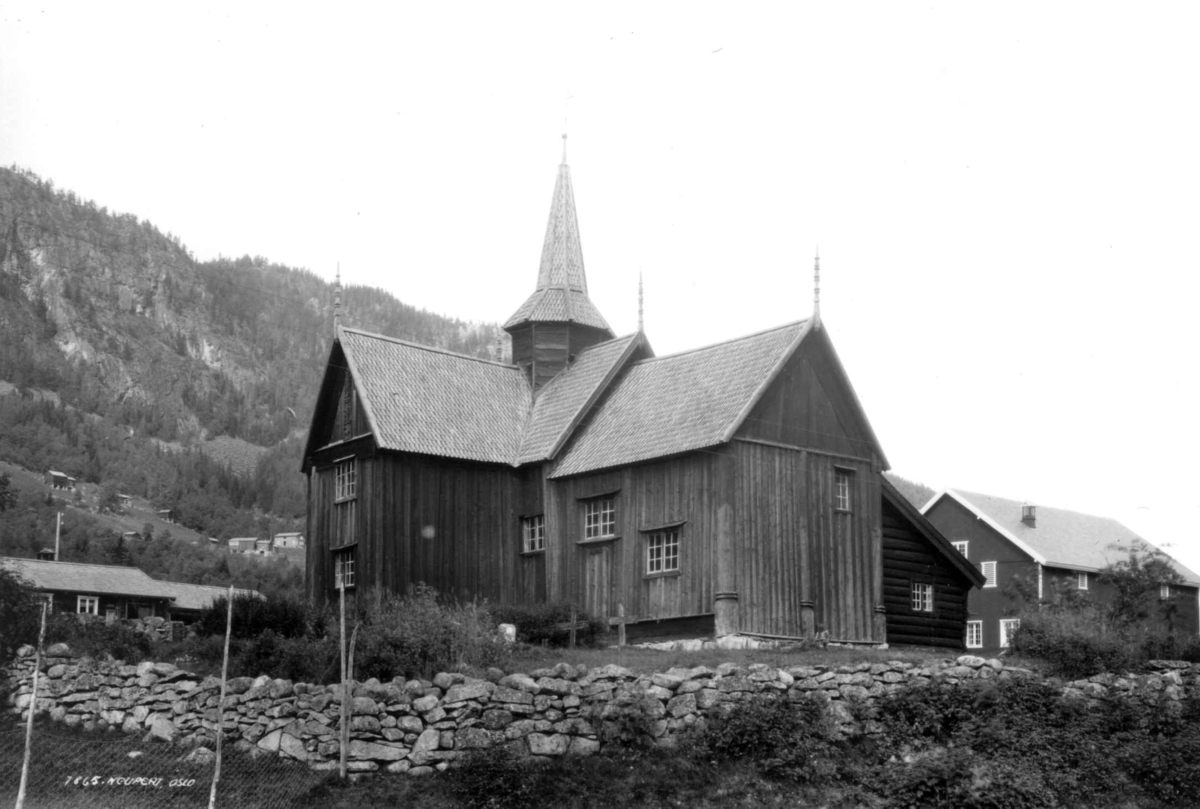 Hermann Christian Neupert, Nore stavkirke, Nore og Uvdal, Numedal, Buskerud. 1930. Kirkegård. Gravkors. Bebyggelse. Gårder, skog og åser i bakgrunnen.