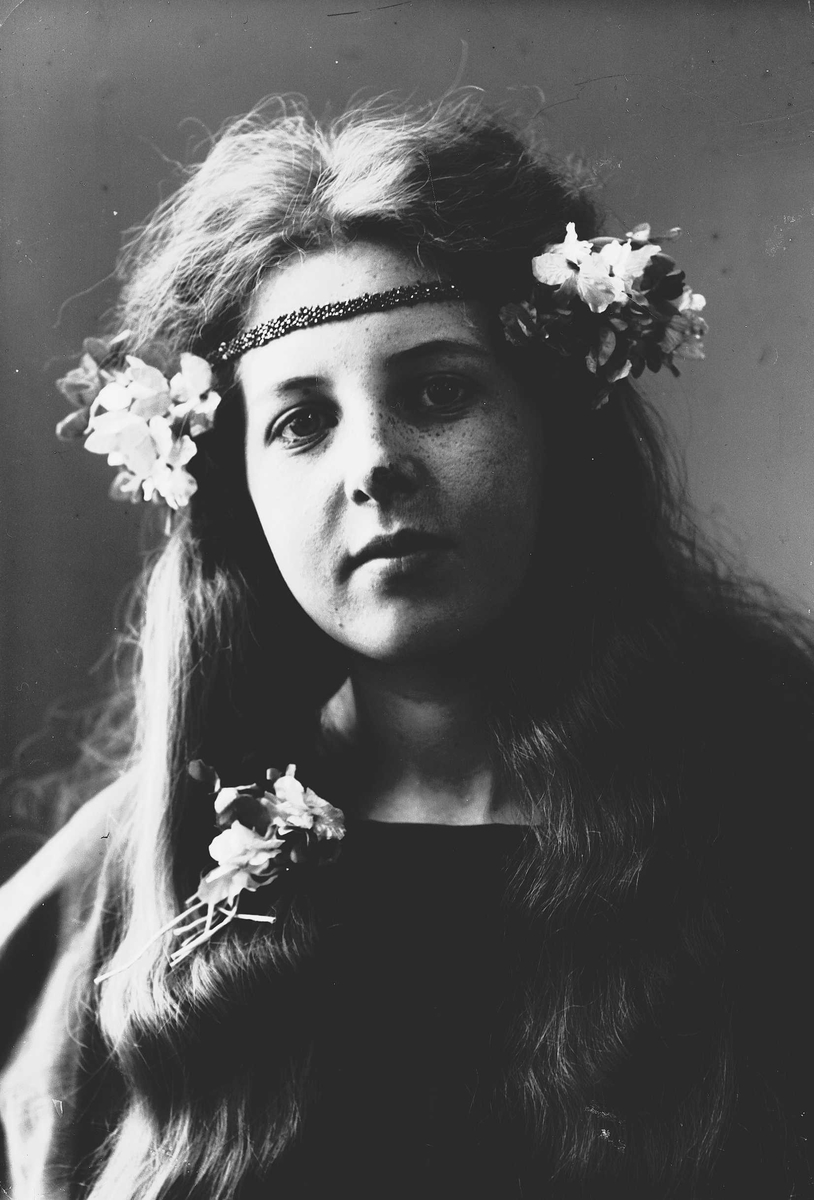 Solveig Lund, Studioportrett av kvinne i kostyme med mørk overdel og blomster i håret.