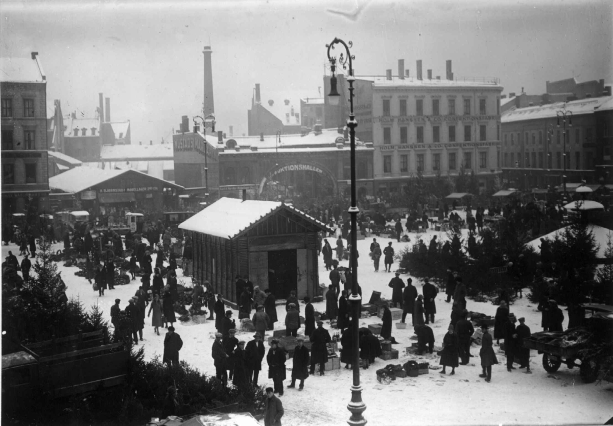Hermann Christian Neupert, Youngstorget, Oslo 1930. Vinterbilde med juletrehandel på torget. Bybebyggelse rundt torget..