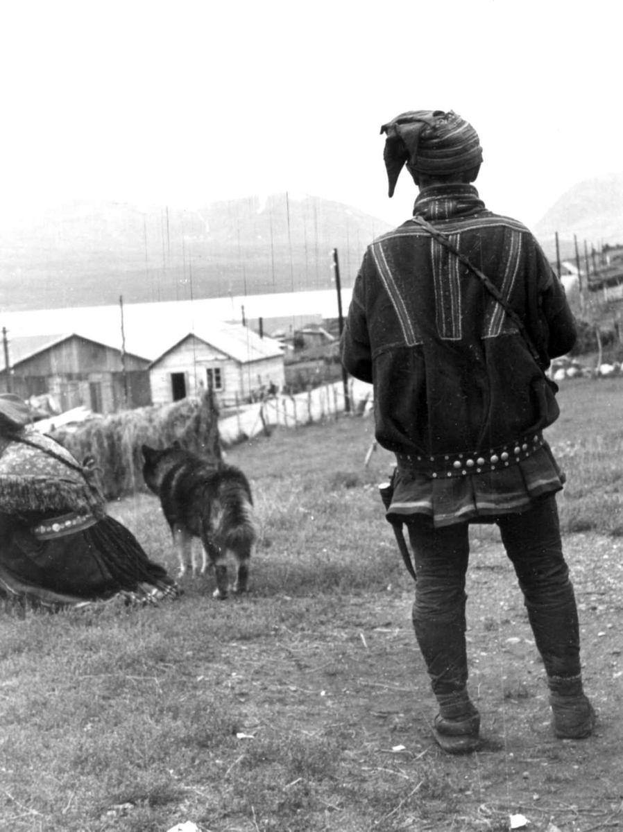 Anna Grostøl, Samer. En same står med ryggen til, bebyggelse i bakgrunnen. Olderdalen, Kåfjord, Troms 1947.