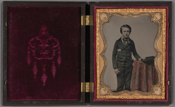 Unknown, [Well-dressed boy standing at draped table with his cap on table top]