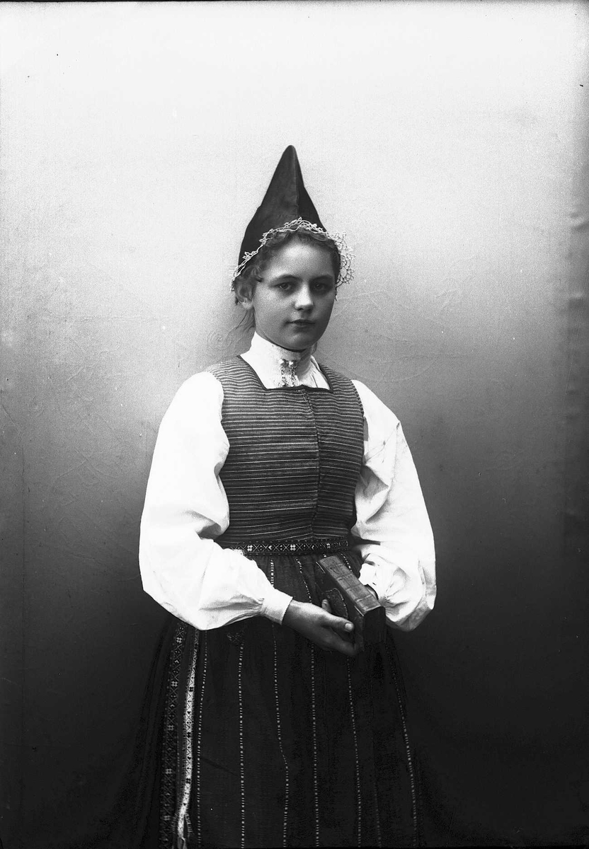Solveig Lund, Kvinne i drakt og lue, som holder salmebok/bibel i hånden.