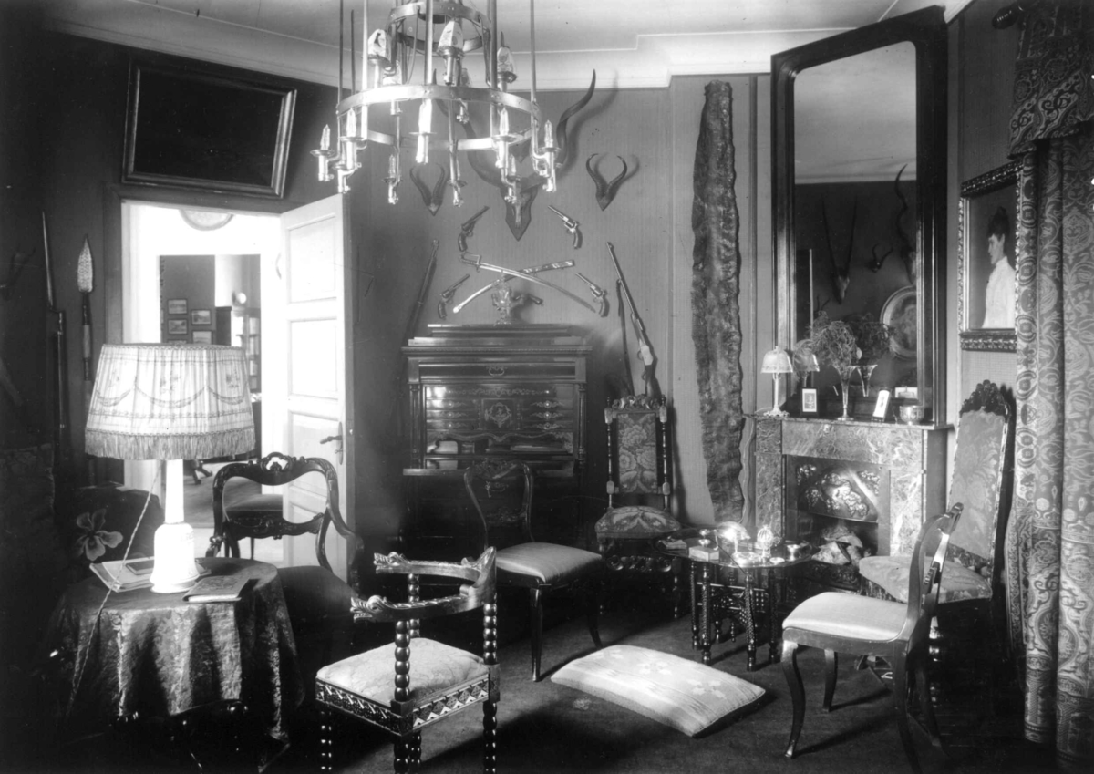 Hermann Christian Neupert, Trapp-Meyer. Interiør fra hall. 1925. Stoler. Bord med lampe. Taklampe. Jakttrofeer. Våpen. Speil. Kamin. Malerier.
