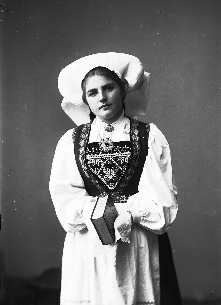 Solveig Lund, Studioportrett av kvinne i drakt og skaut. Hun holder en bok hendene. Bakgrunnen er nøytral.