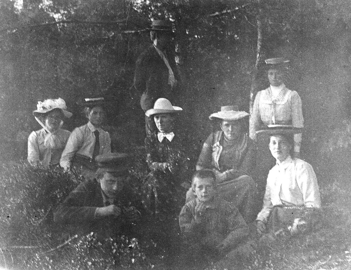 Juliane Fredrikke Langberg, Familiegruppe på veranda i kapellangården Bergenhus i Rakkestad, i anledning botanikkurs. Fotografens svoger, Olaf A. Holm, var res. kap. i Rakkestad 1884-97. Øverst t.v. står lærer Haaken Gran, g.m. prestedatter Margrethe, f. Holm, nederst t.v. Hennes bror Olaf Holm står bak i midten, ved siden av…