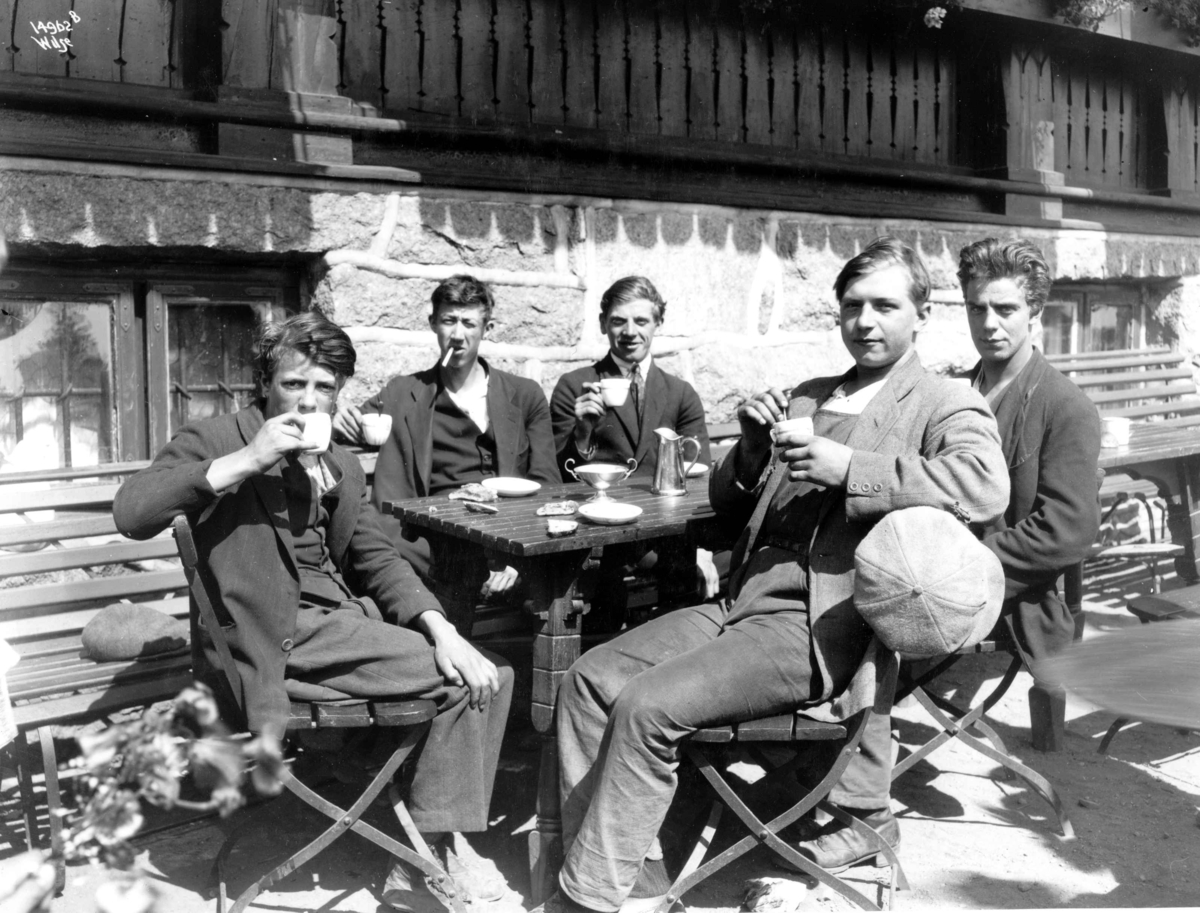 Anders Beer Wilse, Utflukt med Inga Bjørnson. Menn, gutter, i solveggen på Holmenkollen Restaurant, med noe å drikke og en røyk.