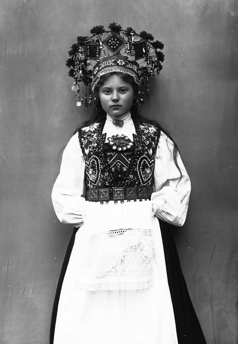 Solveig Lund, Studiofotografi av kvinne med brudedrakt og brudekrone. Stående med klede over hendene. 3/4 dels utsnitt. Frontalt vendt. Ser ut av bildet.