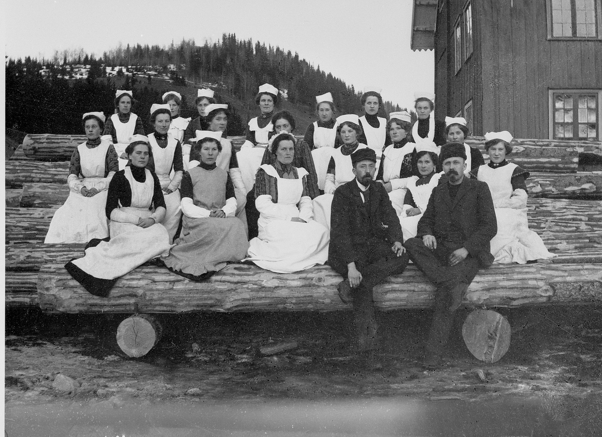 Anno Domkirkeodden, Gruppe kvinner og 2 menn på kokkekurs, Fuglseng, Ringsaker. Sitter på tømmerlunne.