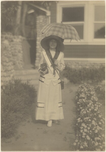 Louis Fleckenstein, [Woman Standing in Front Yard withCamera and Plaid Umbrella]
