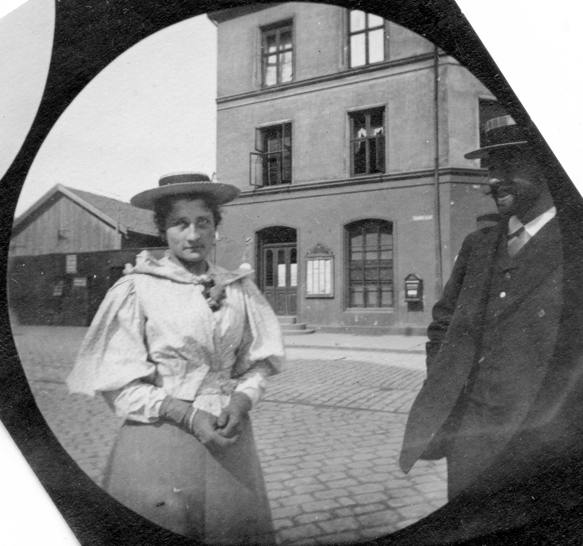 Fredrik Carl Mülertz Størmer, Frk. Collet og professor Thue, senere gift med hverandre, står i bygate. Mur bygård og lave verkstedsbygninger. Postkasse på veggen.