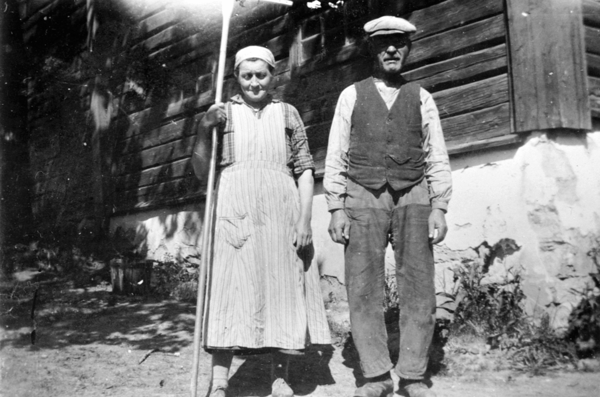 Anno Domkirkeodden, 2 gamle utenfor låven på Hovelsrud, Helgøya. Tea Pedersdatter Maurud (1877-1932) med rive og Olivius Maurud f.1869. Bodde i Tangen fra 1899 til 1920.