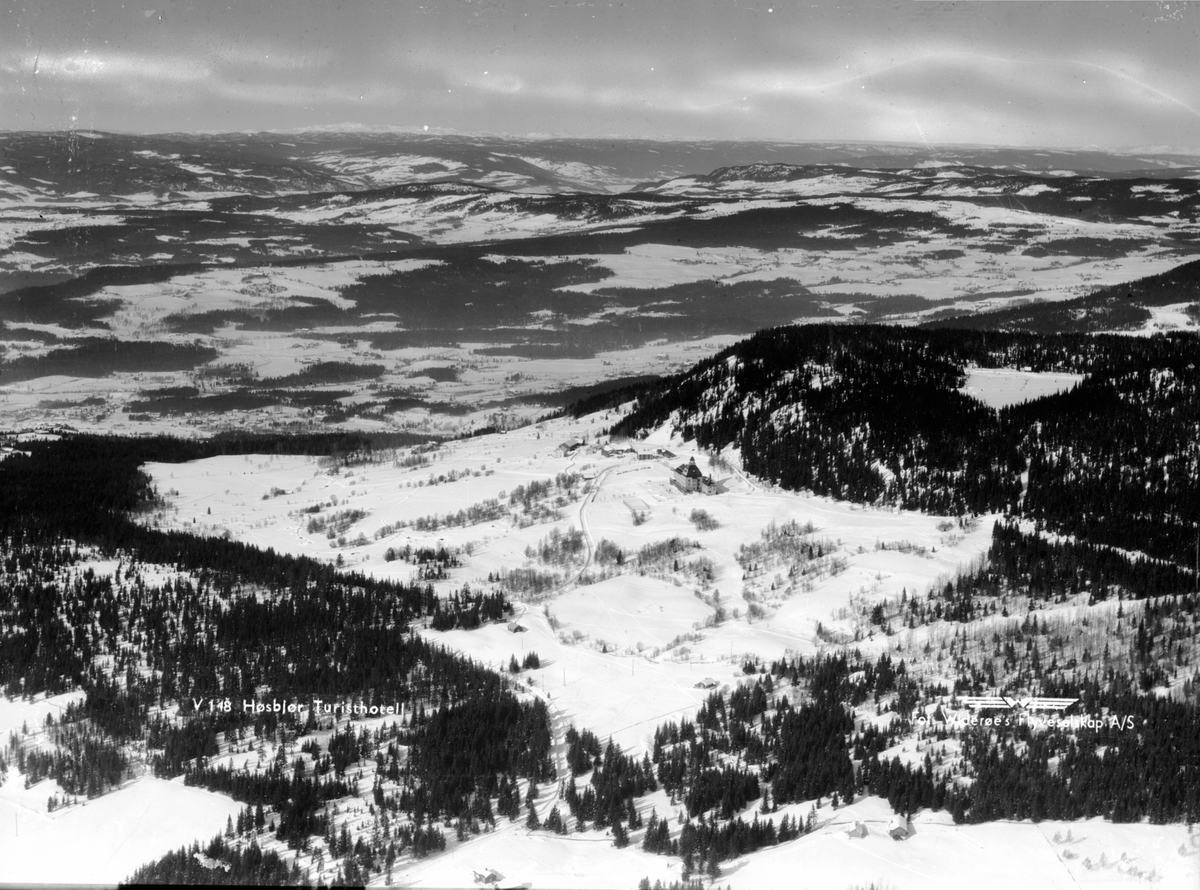 Widerøes Flyveselskap A/S, Flyfoto av Høsbjøråsen i forgrunnen med landskapet mot Veldre, Ringsaker. Vinter.