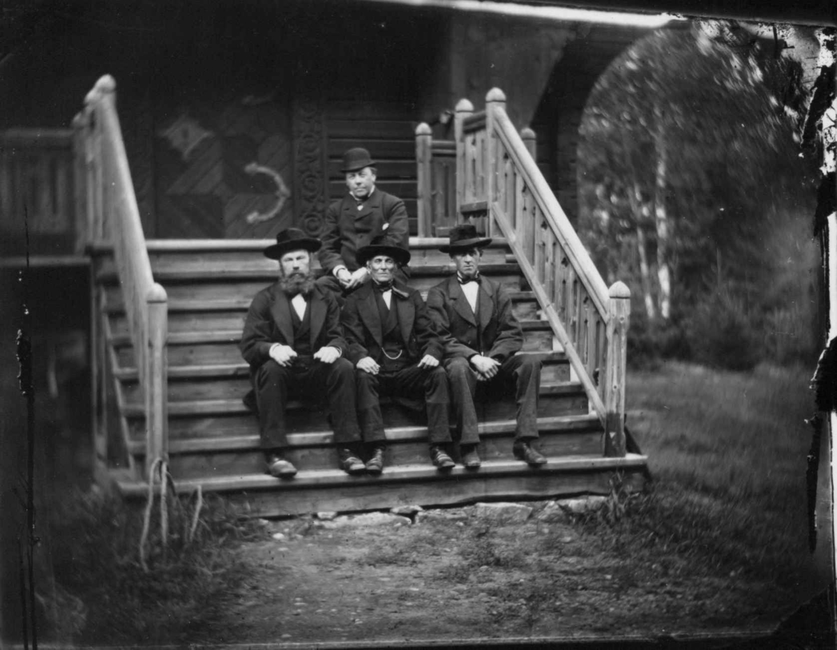 Fredrik Emil Faye, Gruppeportrett, mannsgruppe på trapp utendørs, sittende øverst lensmann Hansen, Ullensaker. Fra portrettserie av personer som bodde på eller besøkte Dal gård, Ullensaker, fotografert av gårdens eier, kammerherre Fredrik Emil Faye (1844-1903) i årene 1875-1900.