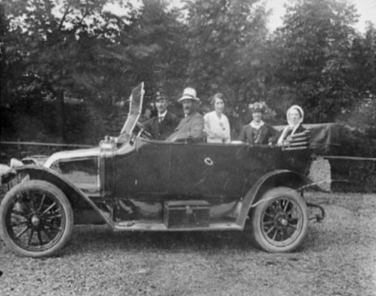Anno Domkirkeodden, 2 MENN, 3 KVINNER, ÅPEN BIL SANNSYNLIGVIS EN RENAULT CA. 1910-14 MODELL, FRA VENSTRE: MARCUS LARSEN, HAMARS FØRSTE DROSJEEIER: AUGUST LARSEN, ÅGOT LARSEN, MARTHA LARSEN, ANNE LARSEN. AUGUST LARSEN KOM FRA SØNDRE OSEN VAR HAMARS FØRSTE DROSJEEIER. BEGYNTE MED SKRAPFORRETNING, BLE VOGNMANN OG SENERE …