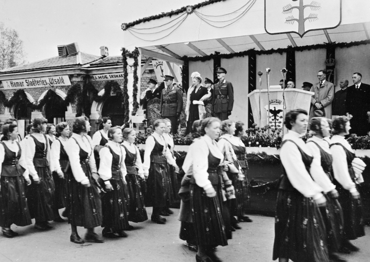 Anno Domkirkeodden, BYJUBILEET 1949, H. M. KONG HAAKON, KRONPRINSPARET PÅ SCENE FORAN BASARBYGNINGEN, BUNADKLEDDE DAMER I FORGRUNNEN