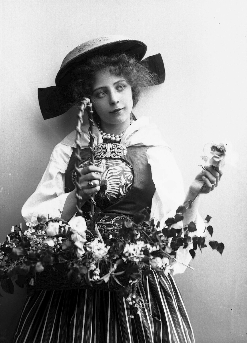 Solveig Lund, Kvinne i drakt og hatt, som holder kurv med grener og blomster.