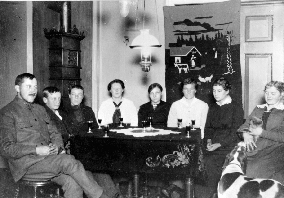 Anno Domkirkeodden, Gruppe personer rundt et bord. Vinglass på bordet. Fra venstre er Even Mengshoel, Kristian Sveen, Hans Sveen, Marie Mengshoel, ukjent, ukjent, ukjent, Agnes Mengshoel.