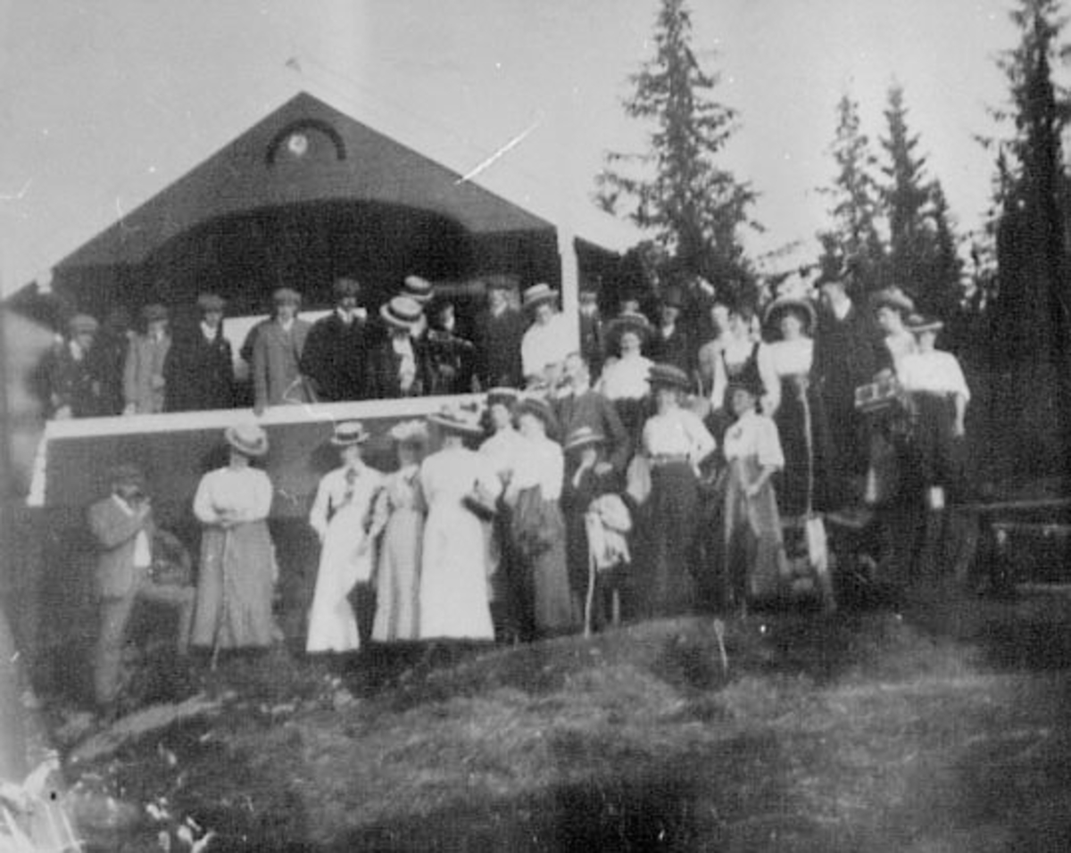 Normann Helger, STOR GRUPPE MENN, DAMER FORAN PAVILJONG, HATTER, KJOLER, DRESSER