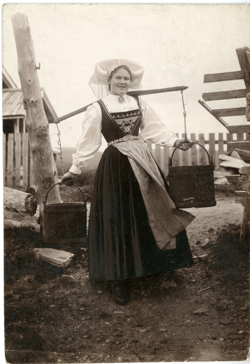 Solveig Lund, Fotografi av kvinne med drakt, på tun med åk og to vannbøtter. Hardanger.