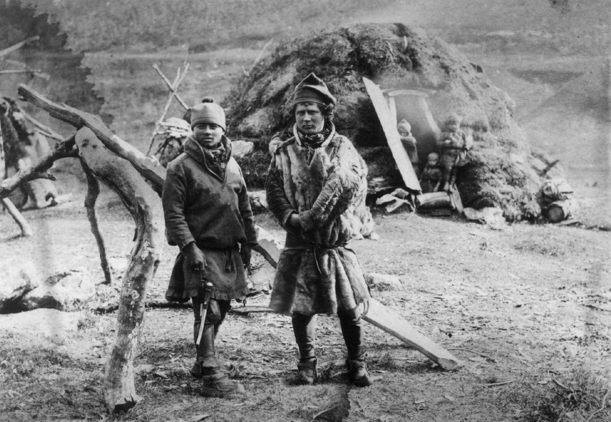 Axel Lindahl, Karesuando-samer på sommeropphold i Lyngseidet. To samer i forgrunnen, gamme i bakgrunnen. Ca. 1884-1890. Fot. Axel Lindahl (nr. 2723).