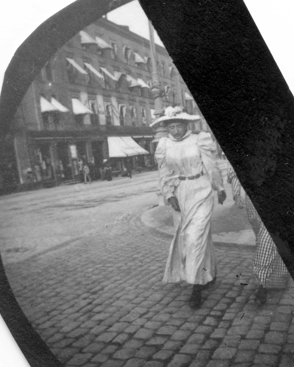 Fredrik Carl Mülertz Størmer, Frk. Ada Lund, senere fru Arnfinsen, Trondheim, spaserer i bygate, butikker på andre siden. Ant. Karl Johans gate, Oslo.