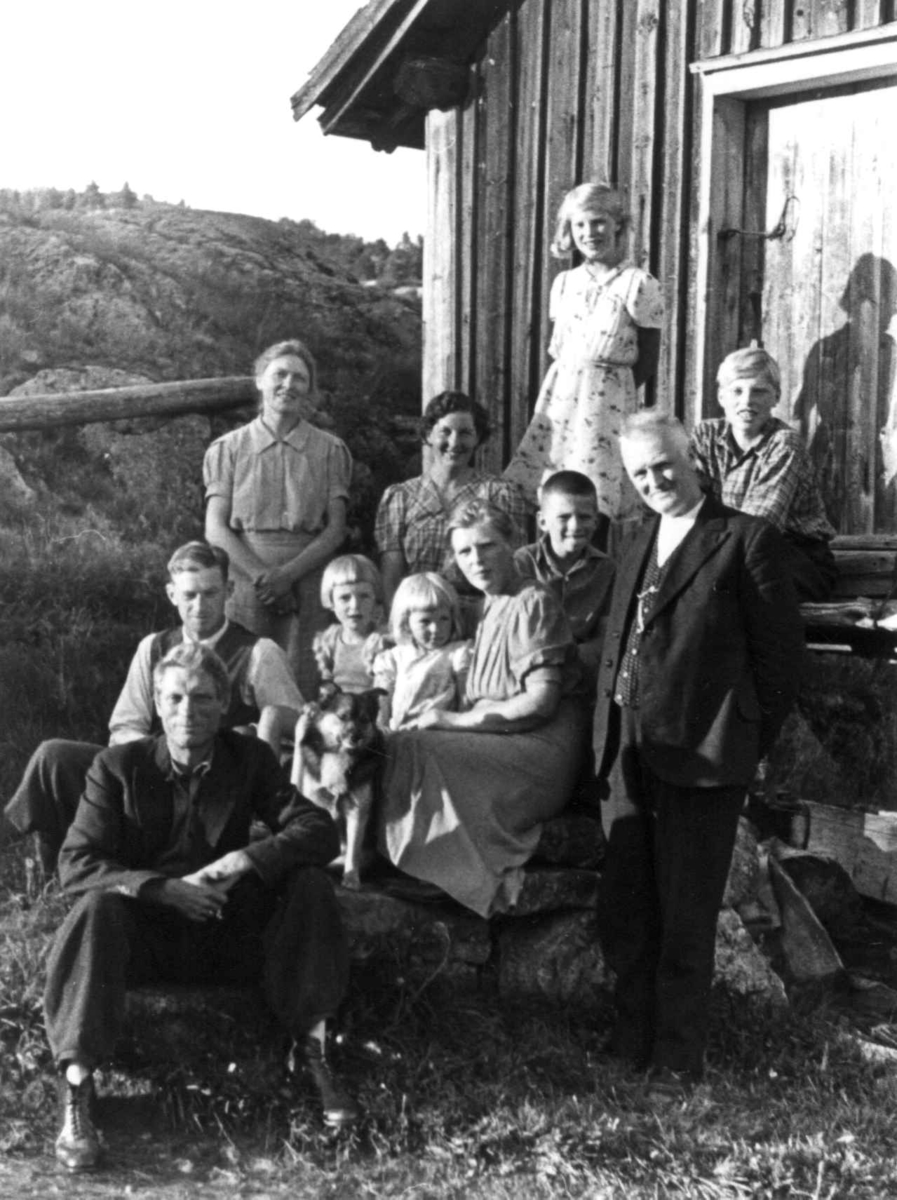 Anna Grostøl, Gruppefoto av voksne, barn og en hund utenfor en husvegg. Fjermedal 1941.