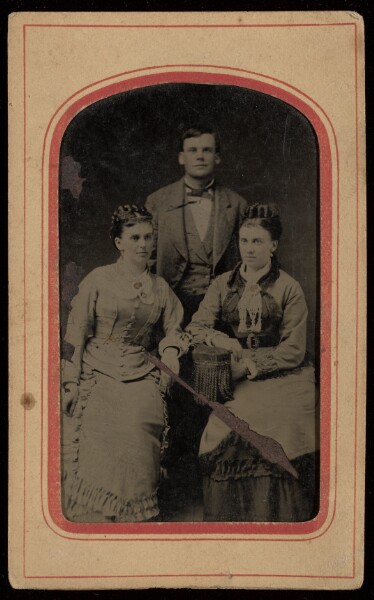 Unknown, [Group portrait: two women seated, one man standing]