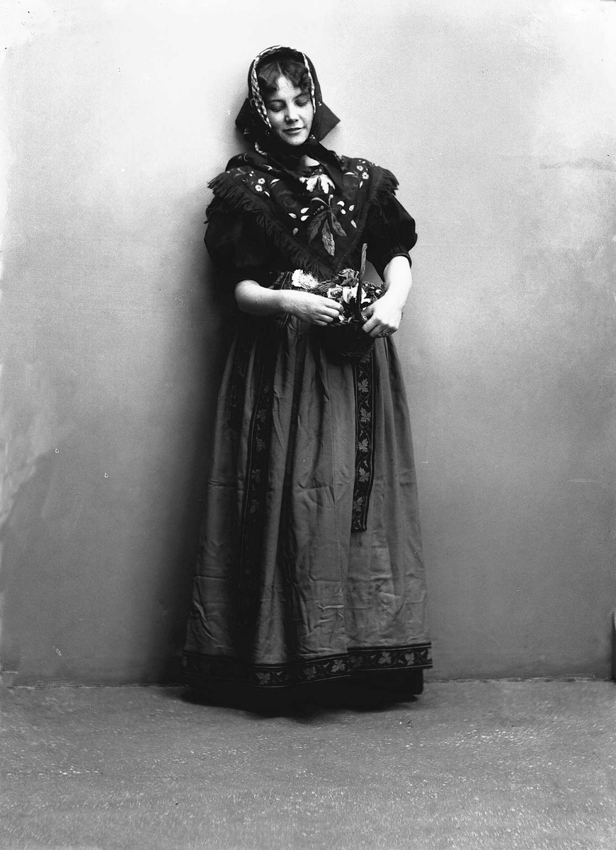 Solveig Lund, Studioportrett av kvinne i drakt og skaut, som holder en kurv med roser i armene. Avfotografert foran en nøytral bakgrunn.