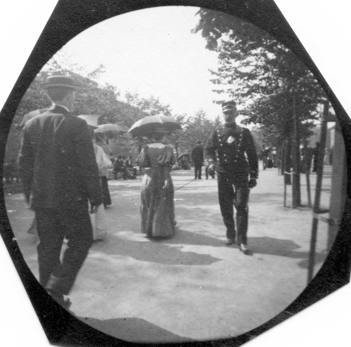 Fredrik Carl Mülertz Størmer, Mennesker spaserer langs Karl Johans gate, Oslo. Mann med dress med ryggen til, damer med parasoller og rittmester Michelet i uniform kommer mot fotografen.