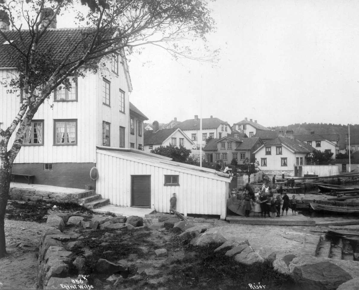 Anders Beer Wilse, Dampskipsbrygga i Risør. Bebyggelse, båter og mennesker ved sjøen.