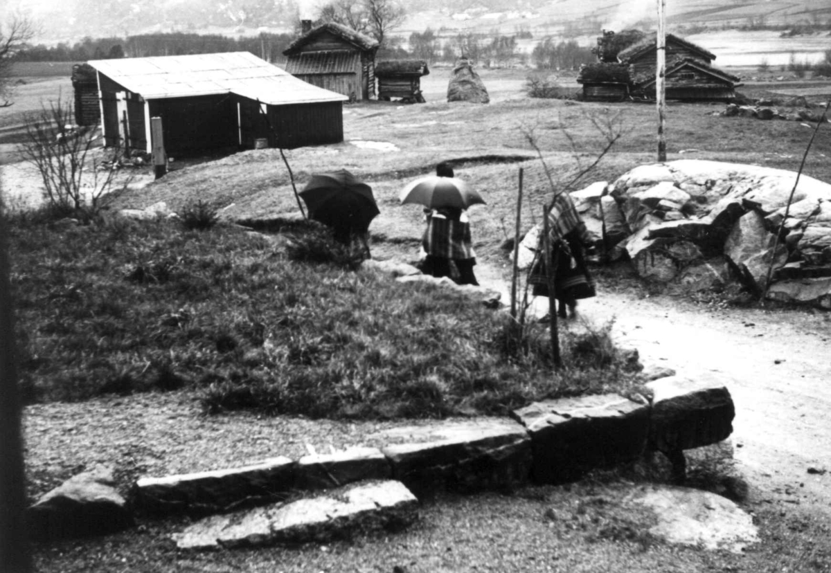 Anna Grostøl, Valle, Aust-Agder 1938. Bededag. Folk med paraplyer på vei til kirken en regværsdag.