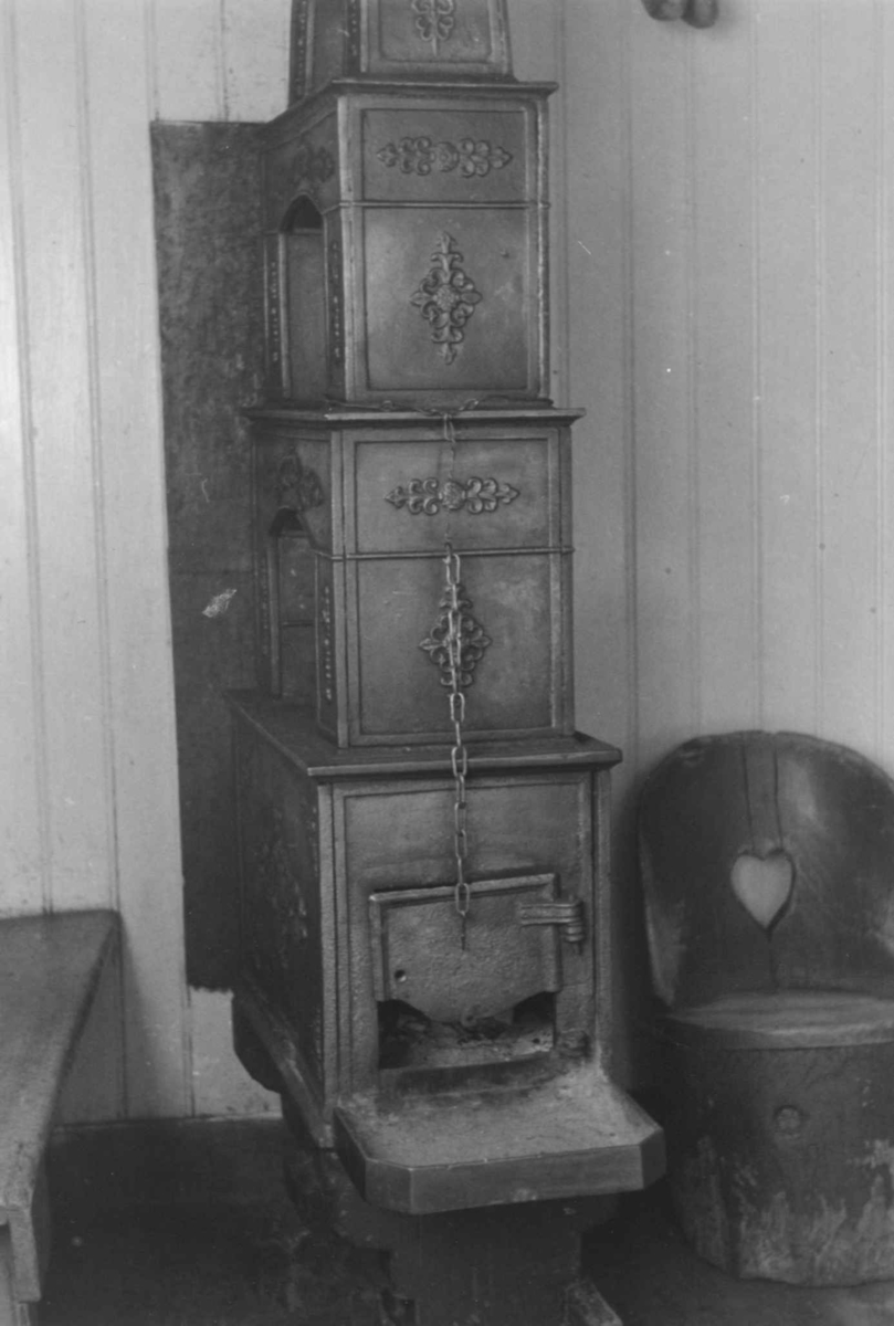 Anna Grostøl, En benk og en kubbestol på hver sin side av en etasjeovn til vedfyring. Åseral, Vest-Agder 1943.