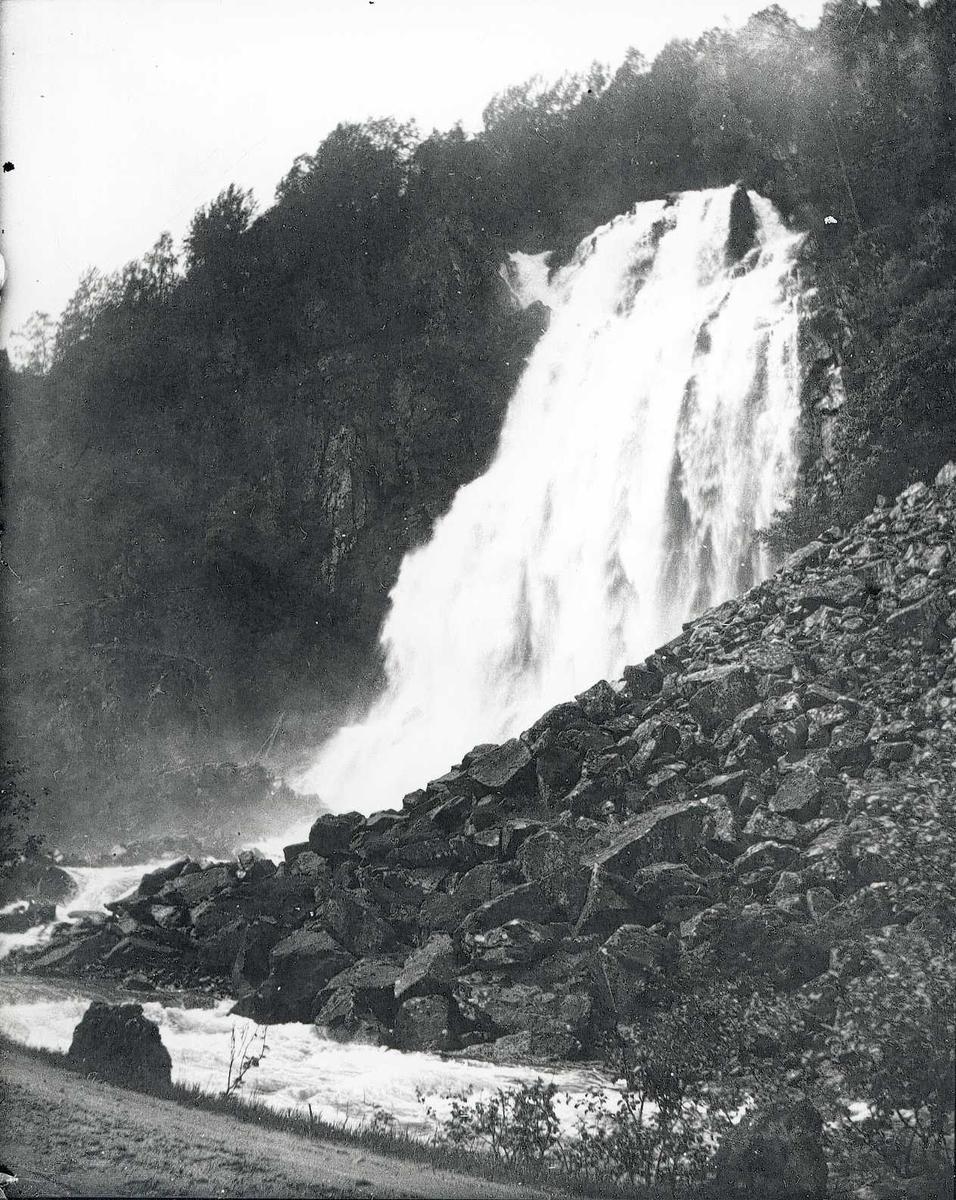 Tom Kent, Foss i fjellside bak steinur, elven renner langs vei med stabbestein.