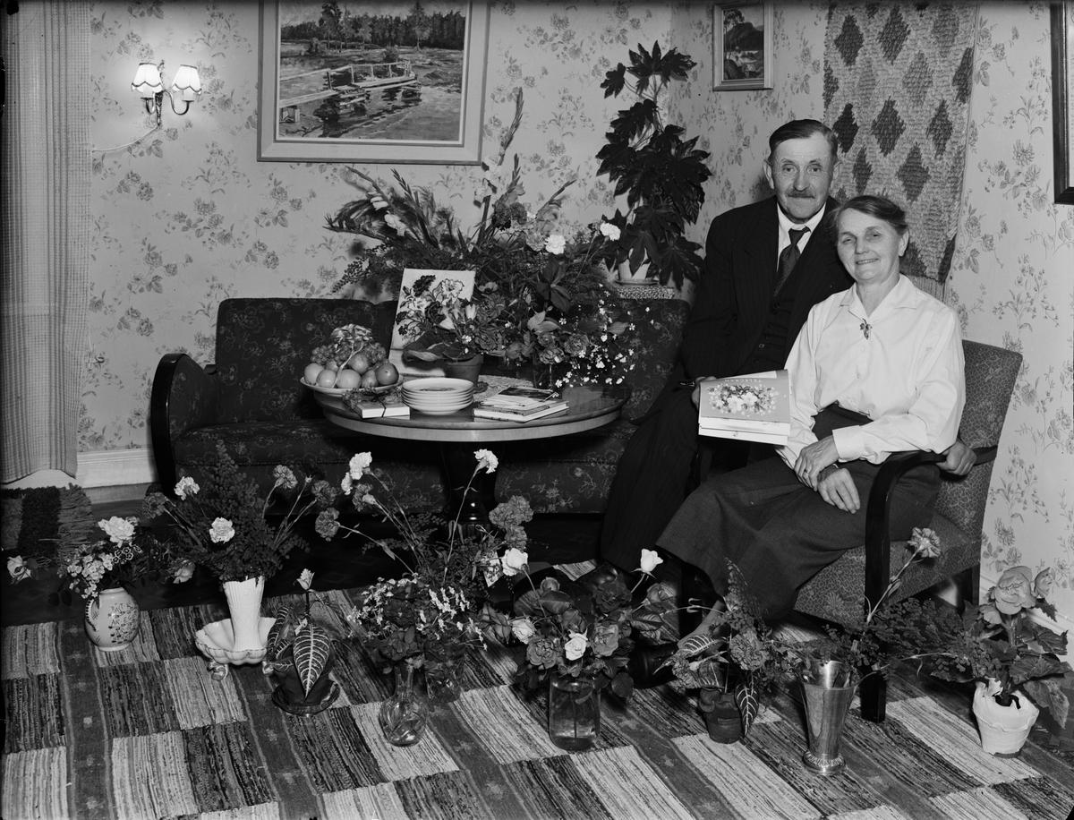 Skötsner-Edhlund, Kvinna och man omgivna av blommor i hemmiljö, Östhammar, Uppland
