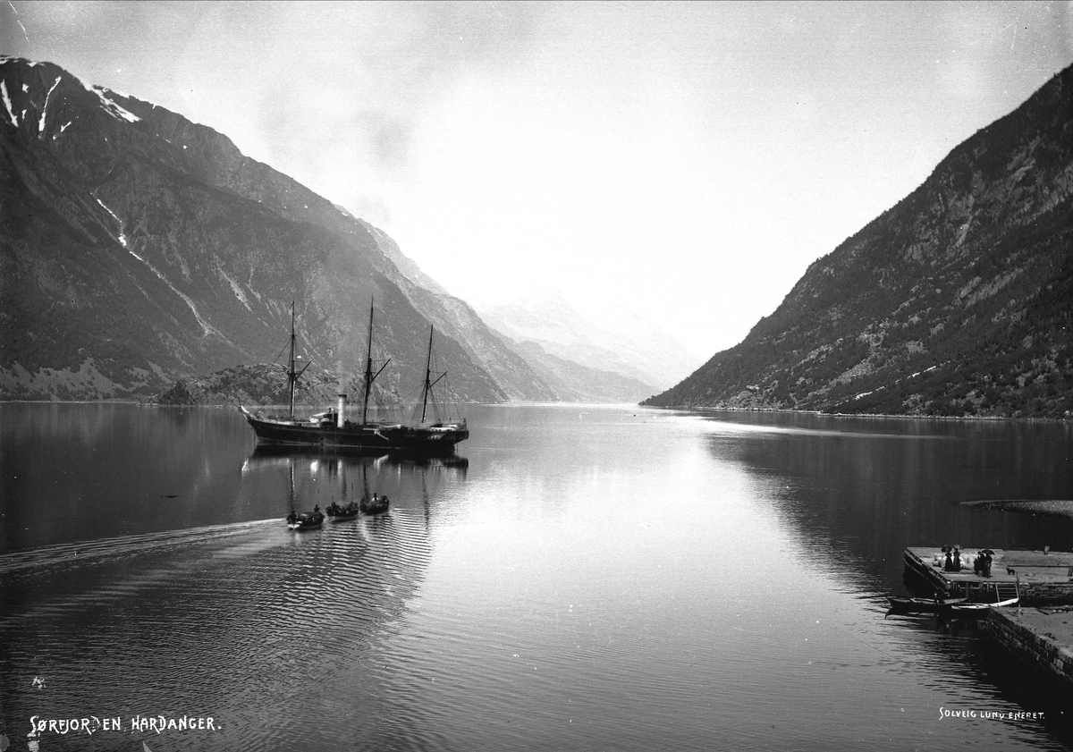 Solveig Lund, Landskapsfotografi fra Sørfjorden i Hardanger. Seil/dampbåt og tre mindre fraktbåter. Til høyre sees tilskuere på brygge.