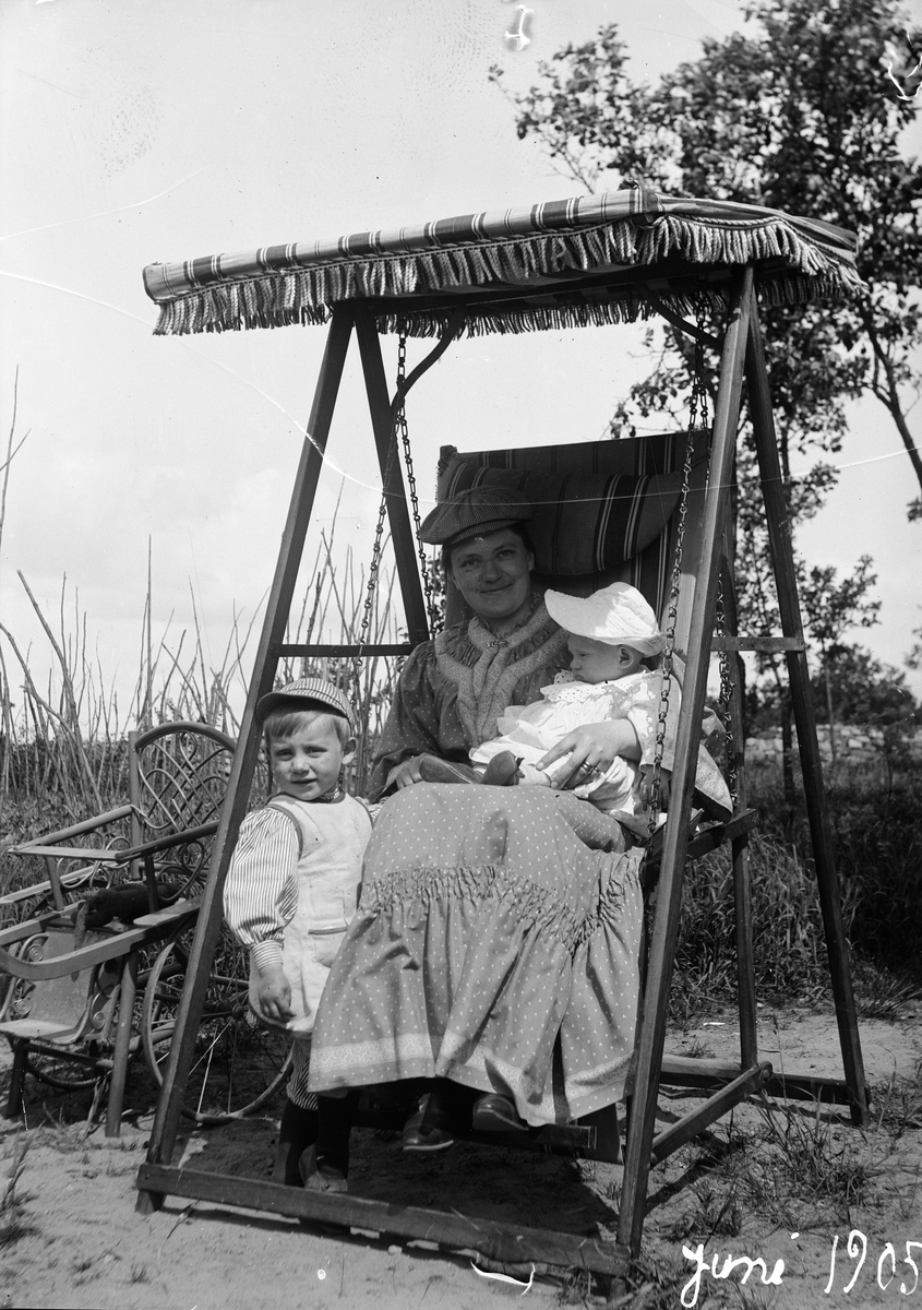 Okänd,, Christine Liljefors med Alf i famnen och Roland bredvid sitter i gungan på strand, sannolik i Sverige, 1905