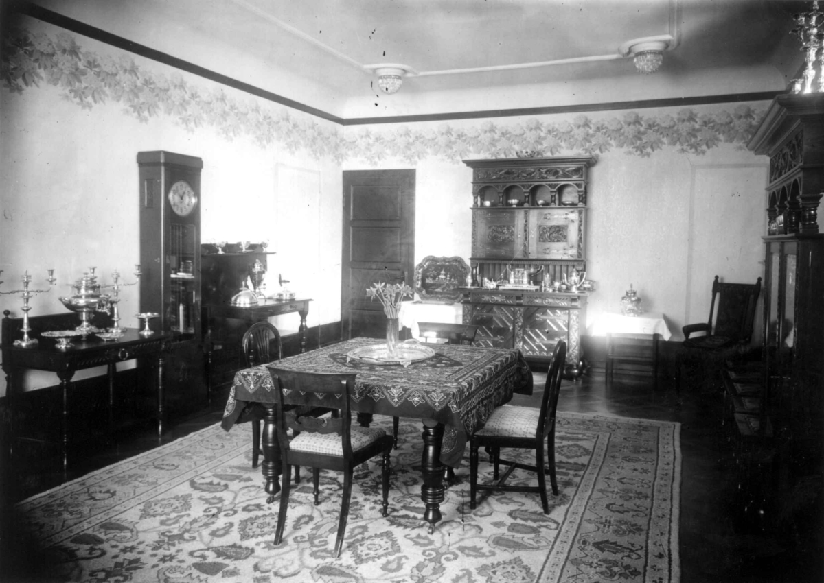 Hermann Christian Neupert, Trapp-Meyer. Interiør fra spisestue. 1925. Spisebord med stoler. Gulvur. Bord med sølvtøy.