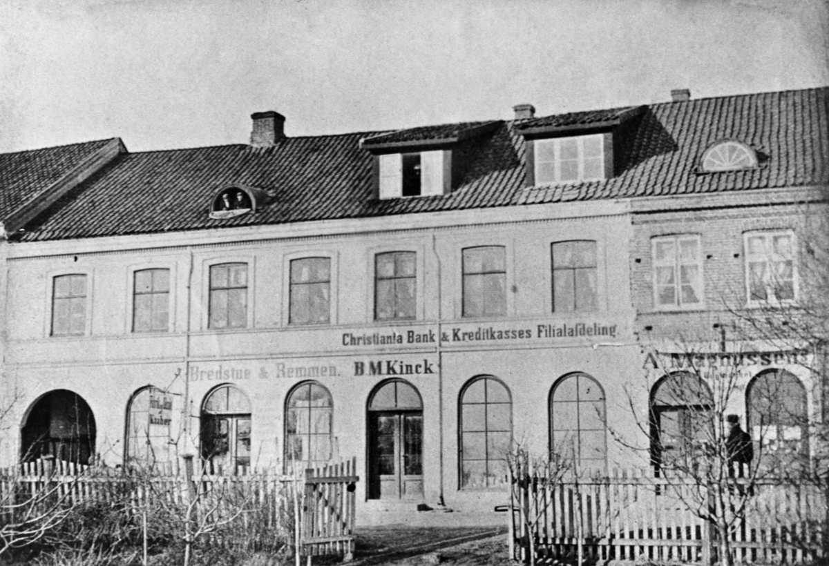 Anno Domkirkeodden, EKSTERIØR: STRANDGATA 51-53 I HAMAR, KINCK, KREDITTKASSEN, MAGNUSSEN GÅRD FØR BRANNEN I 1875. MAGNUSSENS BOKHANDEL, CHRISTIANIA BANK & KREDITKASSES FILIALAVDELING, BREDSTUE & REMMEN, B. M. KINCK FABRIK OG UTSALG AV KÅPER.