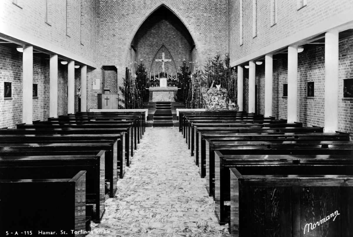 Anno Domkirkeodden, St. Torfinn kirke, Hamar, Katolske kirke, juletid, 1950-årene. Julekrybben står foran Maria- alteret og er omgitt av juletrær. Kirkens utforming som en basilika, med det søylebårede hoveskipet, trer tydelig fraam.